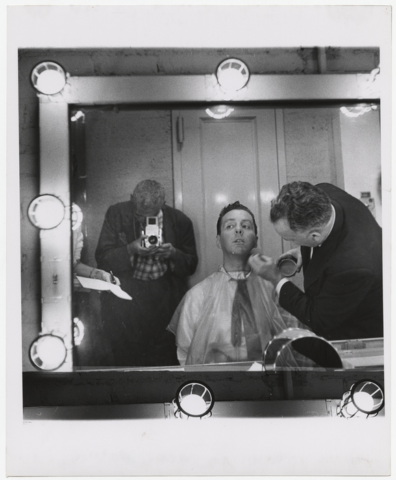 [Weegee photographing Art Ford in a mirror, having makeup applied]