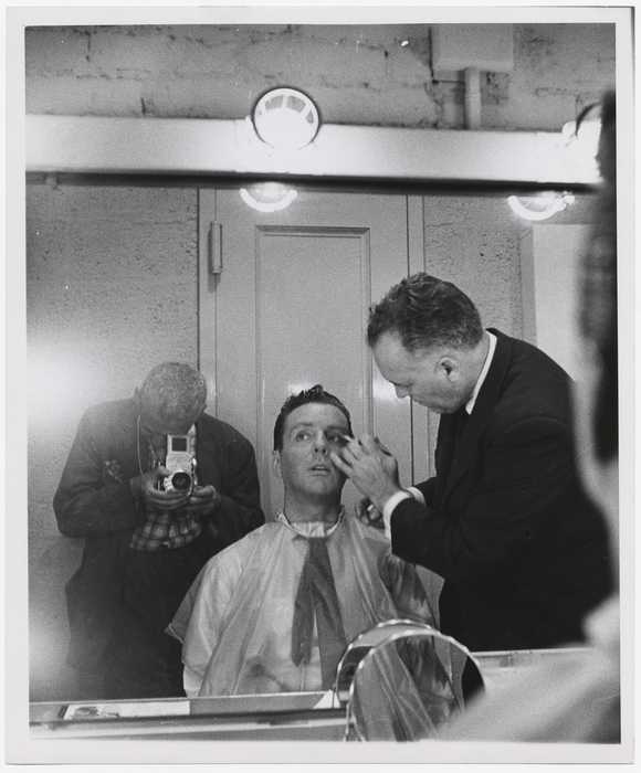 [Weegee photographing Art Ford in a mirror, having makeup applied]