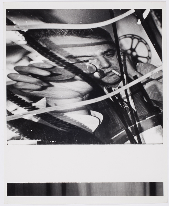 [Weegee having a cigarette in his mouth, looking at some rolls of film]
