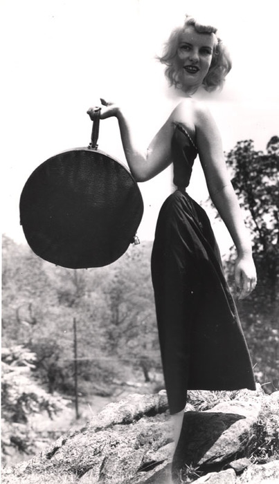 Blonde model on top of a rocky hill with round bag