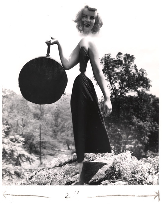 Blonde model on top of a rocky hill with round bag