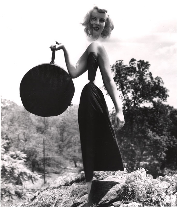 Blonde model on top of a rocky hill with round bag