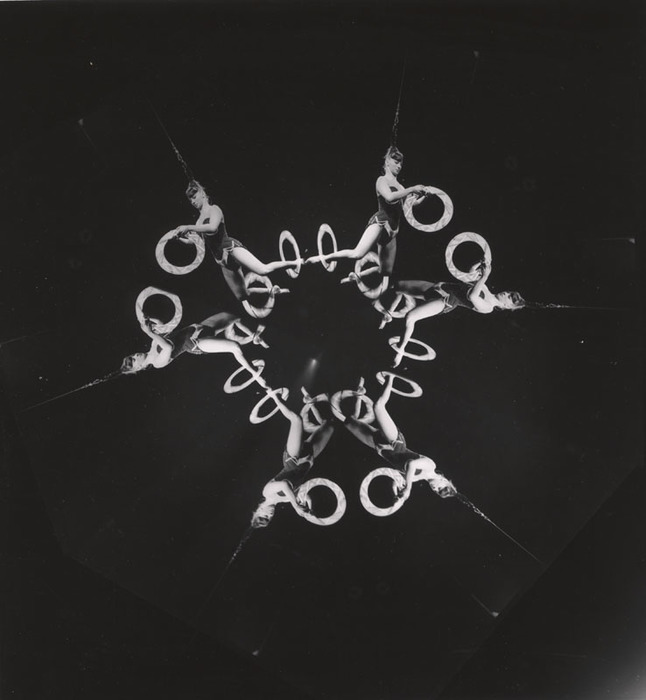 (Acrobat, hanging from her hair, with three hoops)