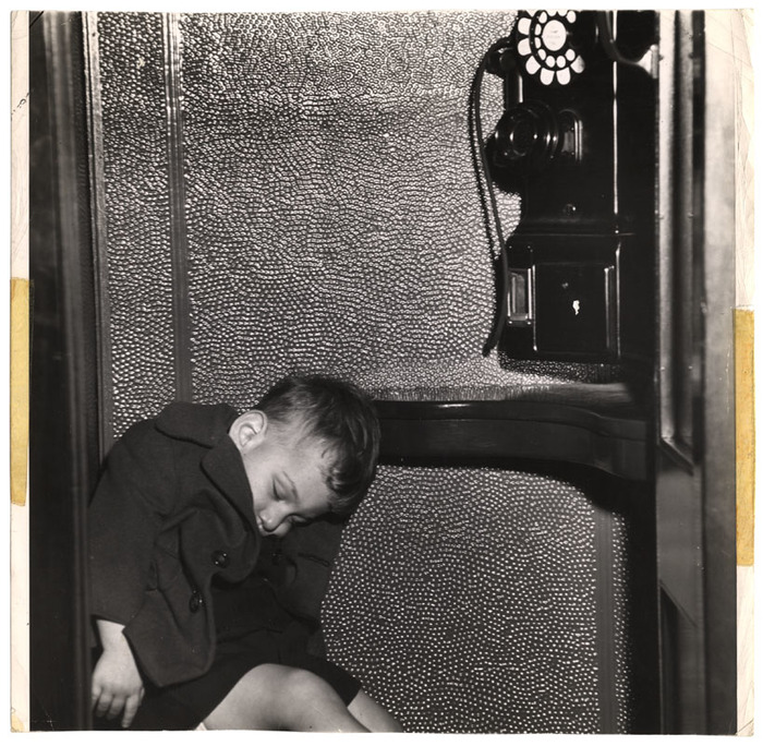 [Boy asleep in telephone booth on Navy Day, New York]