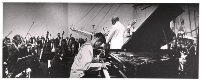 [Widescreen image of pianist, orchestra, and conductor performing on sailboat Christian Raditch in Louis de Rochemont's film "Windjammer"]