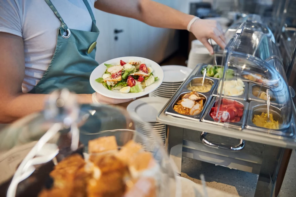 A cafe employee dishes up a salad using ingredients in a chafing dish behind the counter.