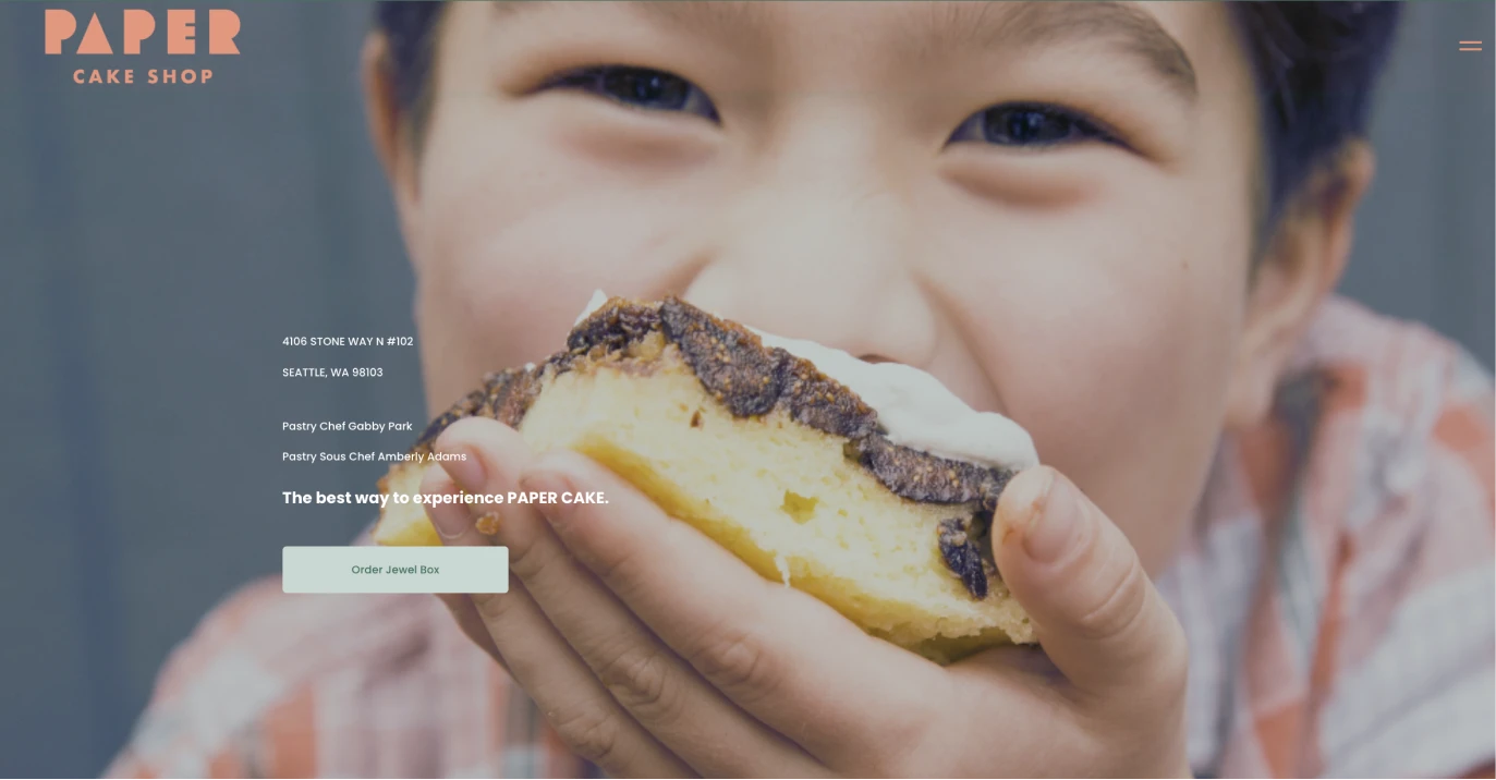 A website screenshot displaying a close-up image of a boy eating a cake slice with text that reads, "Paper Cake Shop" and additional details with color accents in hunter green, coral pink, and mint green.