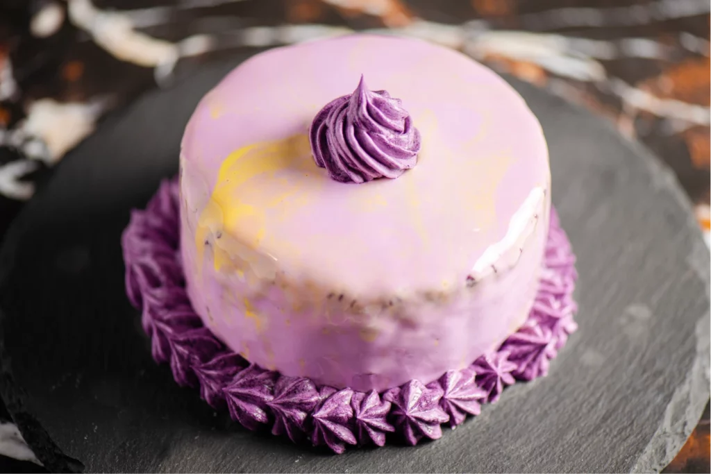 A purple ube cake decorated with purple swirls and yellow marbling, set on top of a stone display plate.
