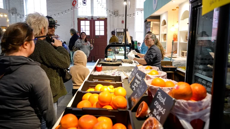 Customers line up at Charles Family Farm's booth next to a variety of oranges, including Minneola and blood oranges.