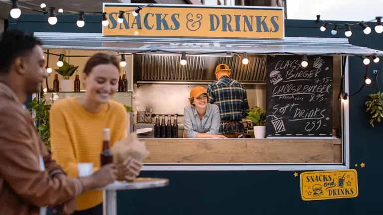 Black and yellow snacks and drinks food truck with a smiling employee and customers eating in the foreground.