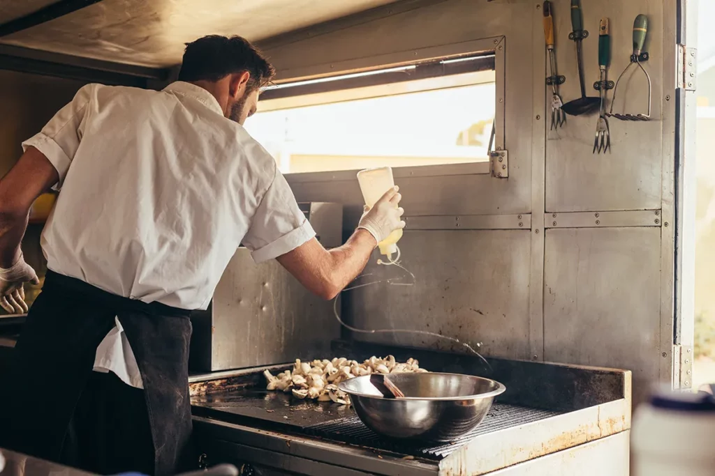 A male chef grills meat inside a food truck kitchen.