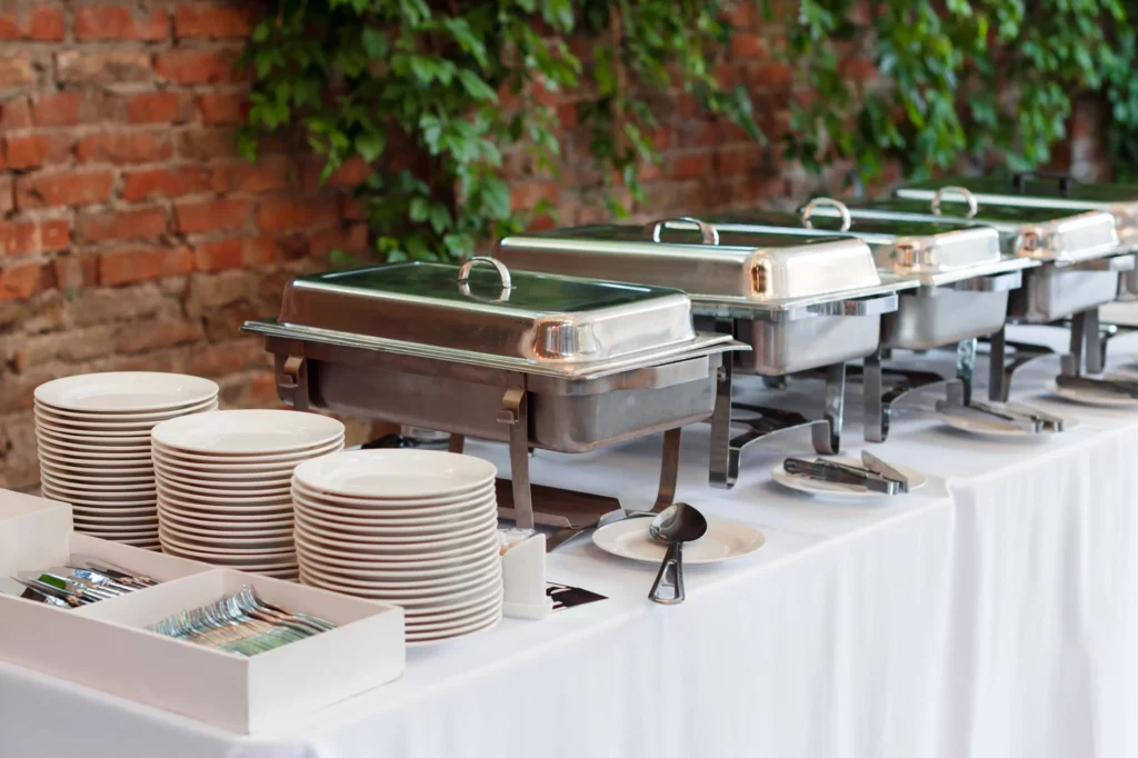 buffet style catering setup with flatware, plates, chafer dishes, and serving utensils