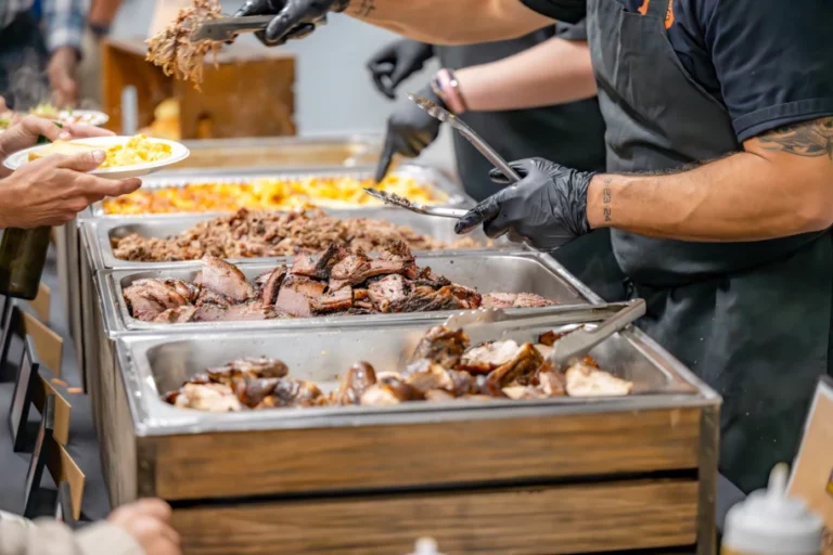 catering service workers serve barbecue to guests out of hotel steam pans