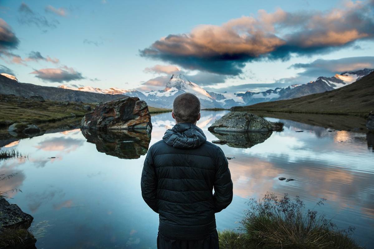 Man looking out over an alpine lake, snow-capped mountains in background