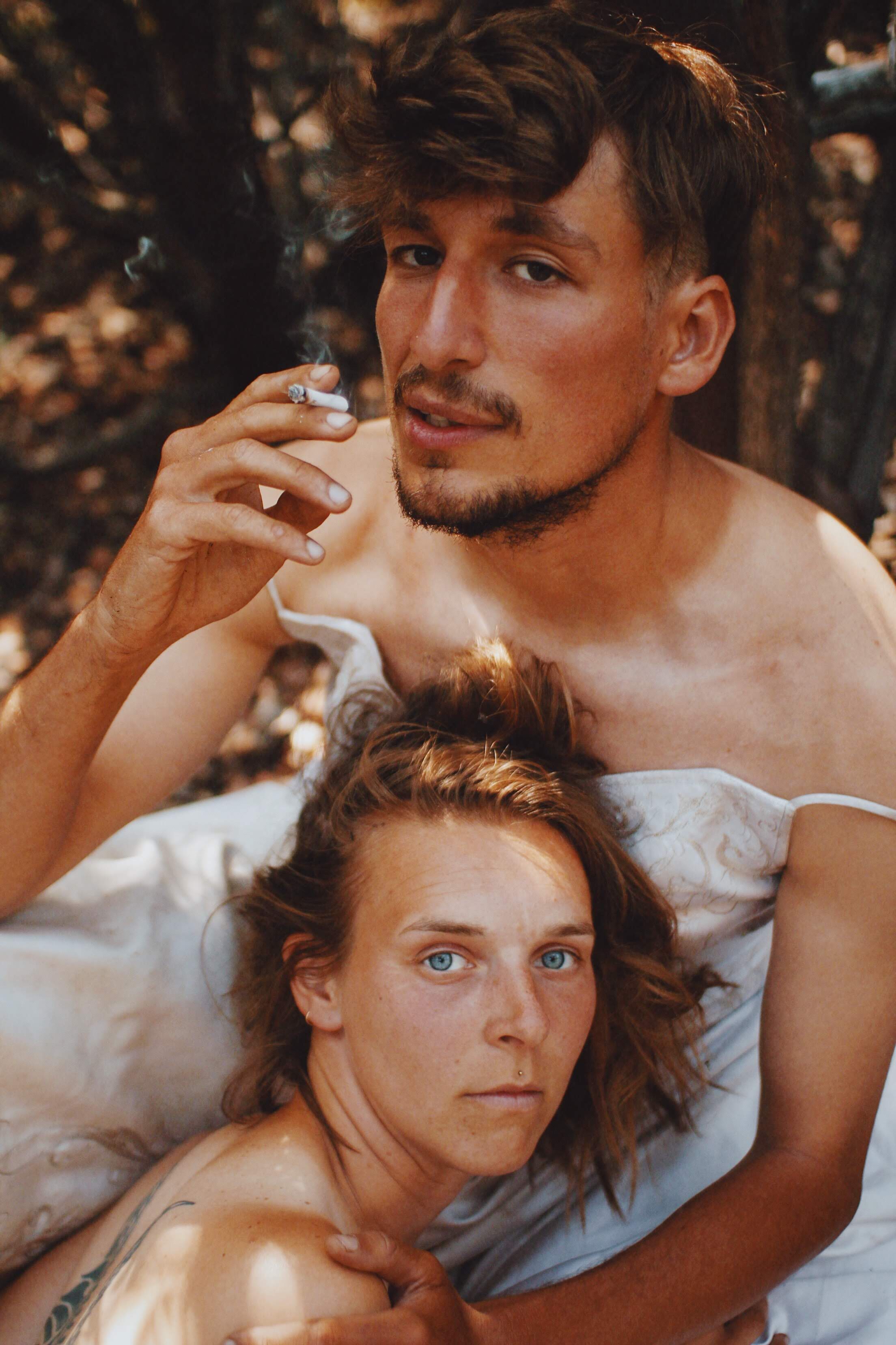 Man in a dress smoking cigarette with hand on woman's shoulder Man in a dress smoking cigarette with hand on woman's shoulder