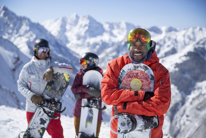 3 snowboarders pose with their boards atop a peak in Aspen, Colorado