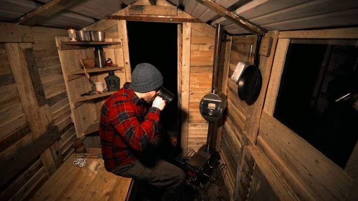 man sitting in a hand built pallet wood cabin