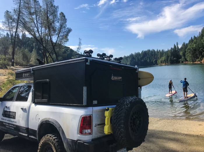 truck parked in front of lake with stand-up paddleboarders in background