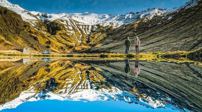 male and woman standing at shore of lake with mountain reflected in lake