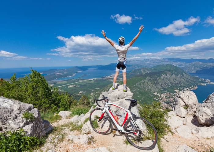 man standing on mountain top with arms outstretched with his bike nearby