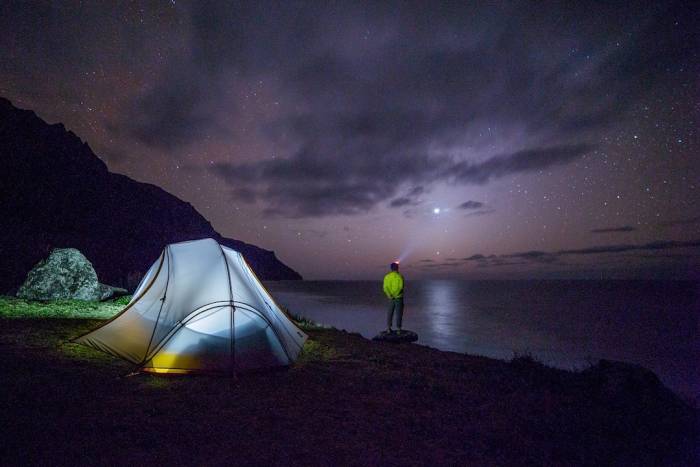 man in green jacket with headlamp looking up at stars at night