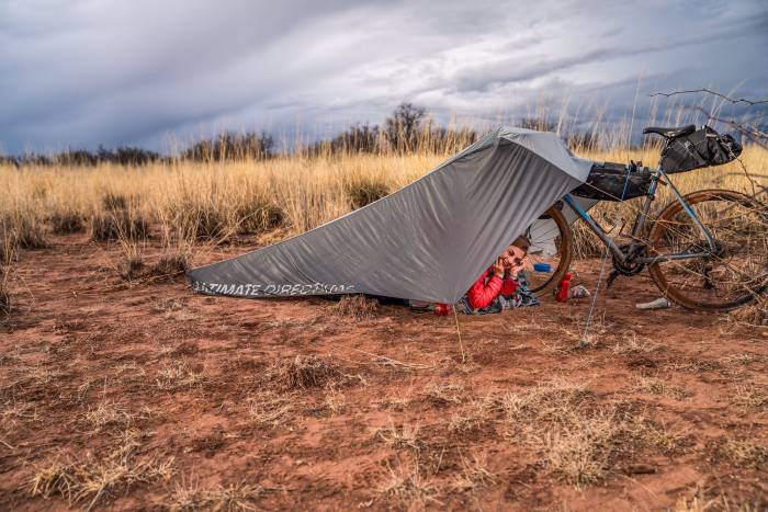 woman camping under Ultimate Direction Bike Tarp adjacent to her bike