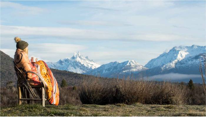 Woman in camp chair curled up in Rumpl blanket looking out at mountains