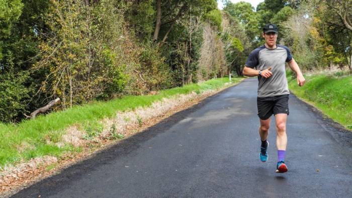 Beau Miles running on pavement lined with grass and trees