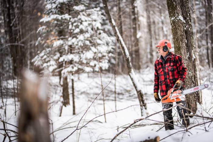 Gary Edinger in flannel carrying electric saw through forest