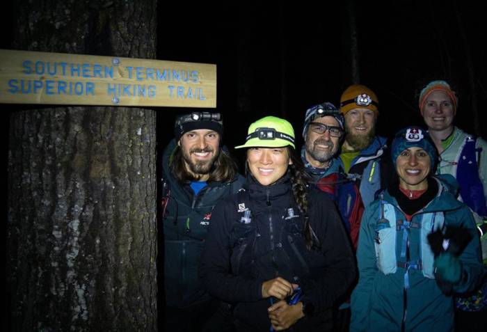 Alex Elizabeth and crew smiling at night next to southern terminus trail sign