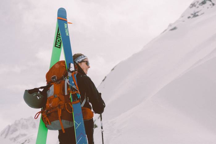 female skier with red pack carrying Faction Agent Series Skis in a-frame orientation
