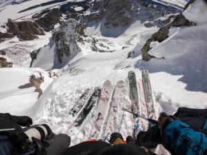 three pairs of skis lined up on edge of steep slope looking down