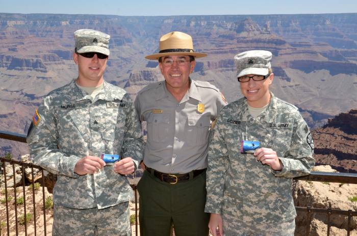 two military members and one ranger smiling at camera and holding up park passes at Grand Canyon National Park