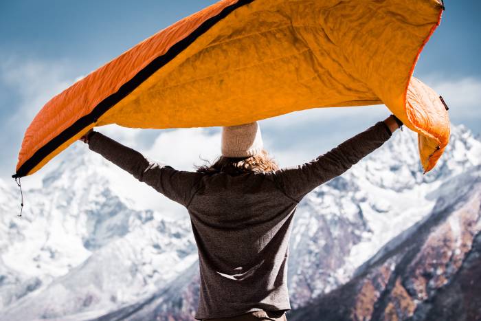 person with arms outstretched holding up Enlightened Equipment quilt in the wind in the mountains