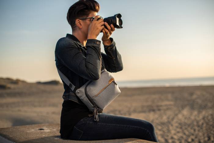 photographer on a beach holding up camera to face wearing Peak Design Sling Bag at side