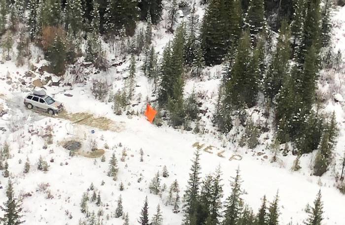 SOS message of "HELP" spelled out in snow near orange flag and white car