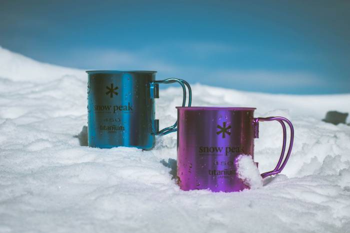 Snow Peak branded neon titanium mugs resting in snow