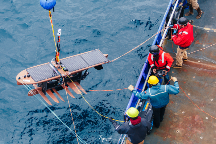 workers on barge lowering The Wave Glider surfboard down in the ocean