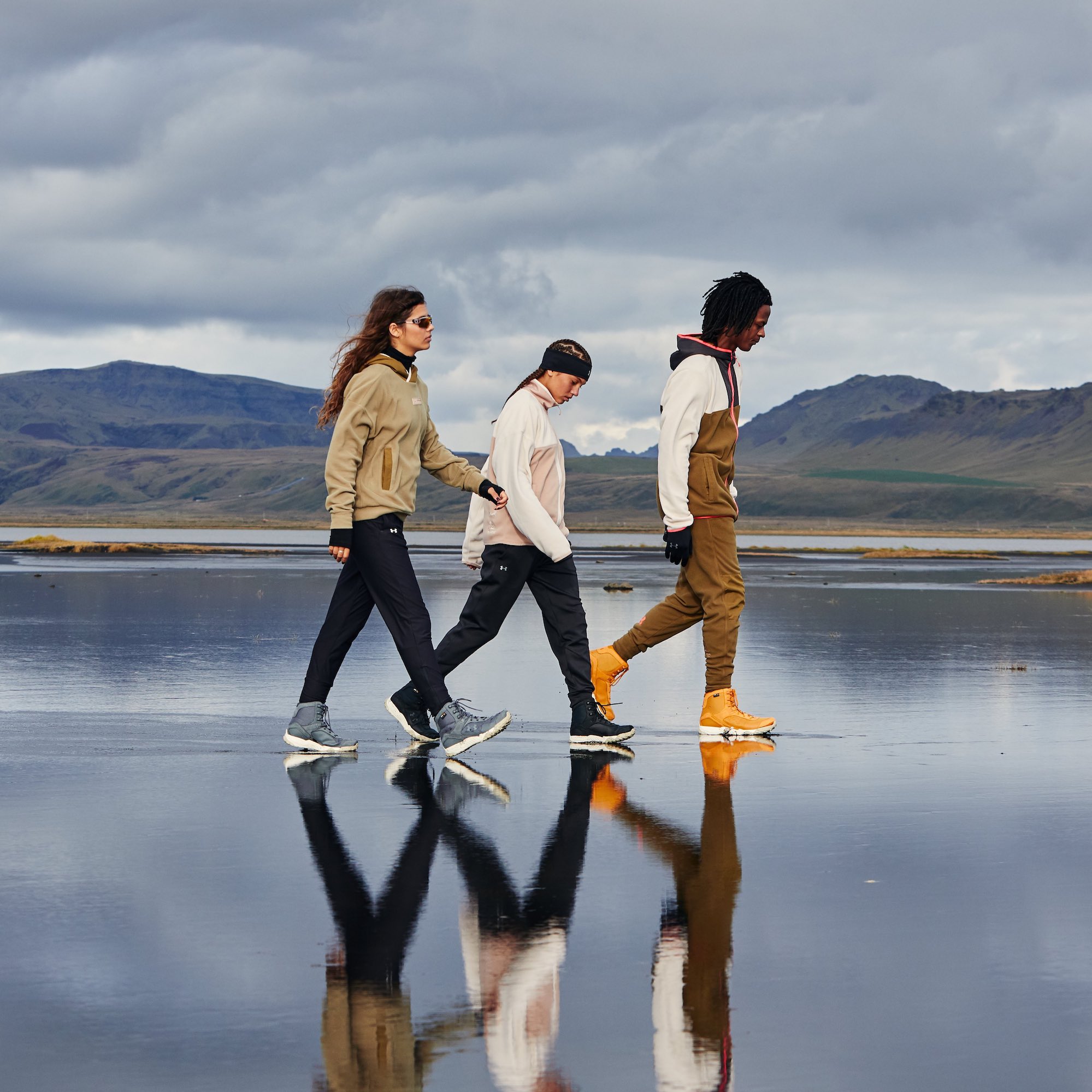 3 people wearing Under Armour Trek Pants walking across glassy surface with mountains in background