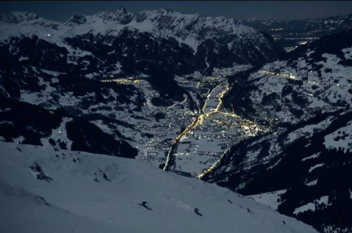 skiers traverse above moon-lit town in night skiing film