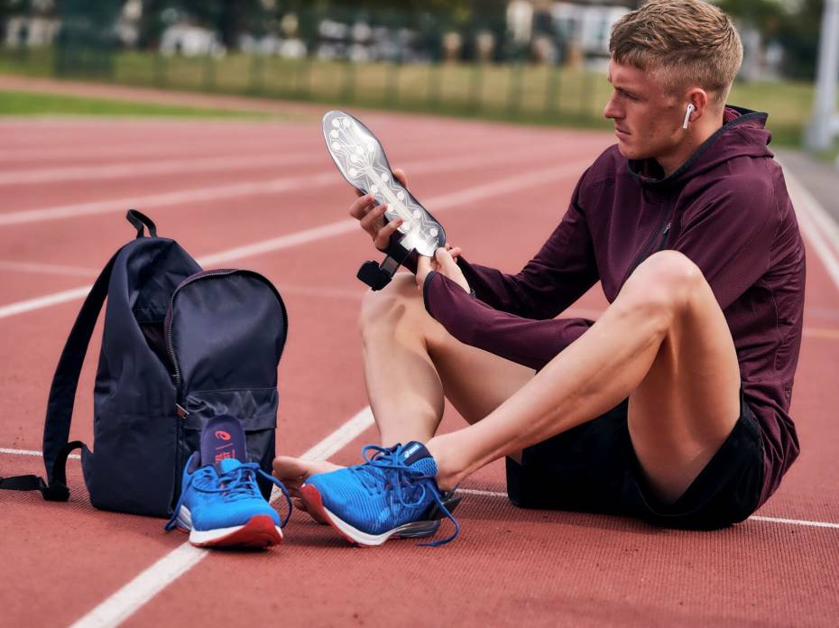 Smart Soles: NURVV Creates Biometric Inserts for Running Man sitting on track wearing earbuds and putting on NURVV Run biometric and app-connective Insoles