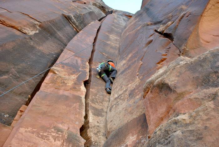 Mary wearing gray pants and orange shirt, crack climbing on toprope in Indian Creek