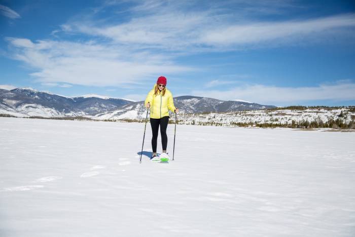 woman in red beanie snowshoeing with crescent moon across flat snow