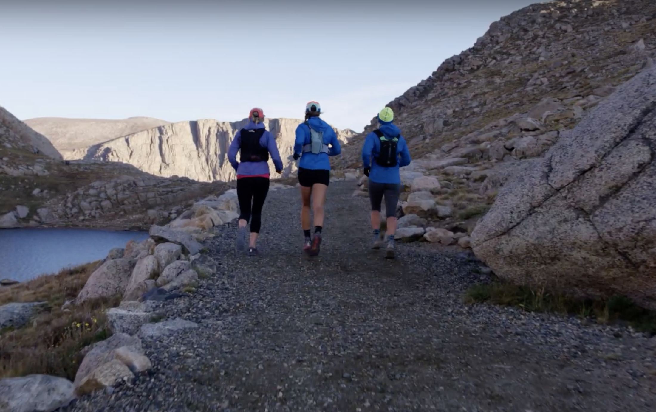 3 females runners with packs running down gravel trail away from camera