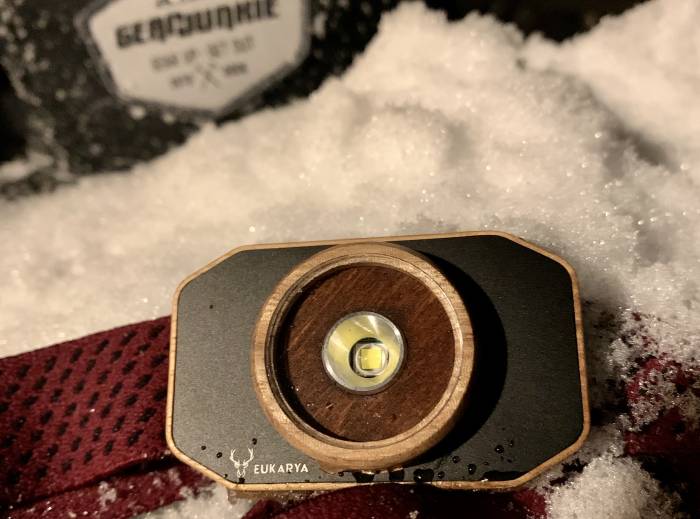 Eukarya origin wooden headlamp with red strap resting in snow