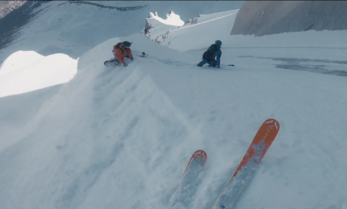 point of view freeskier descending powdery couloir with two skiers below