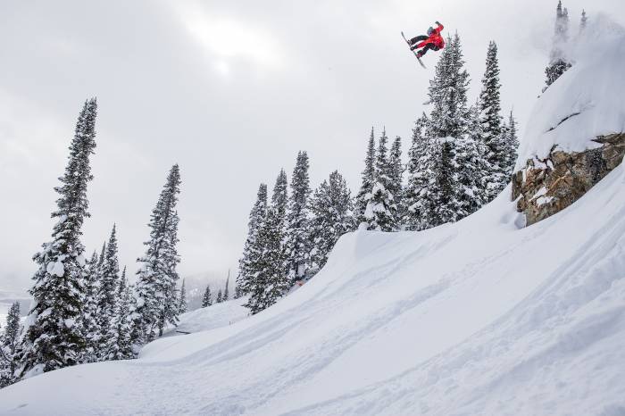 snowboarder in red jacket flying off jump in right of photo at Natural Selection Tour practice session