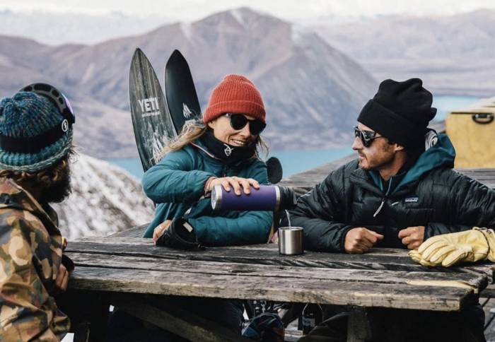 3 skiers in sunglasses looking over mountains, one pouring drink from purple YETI bottle