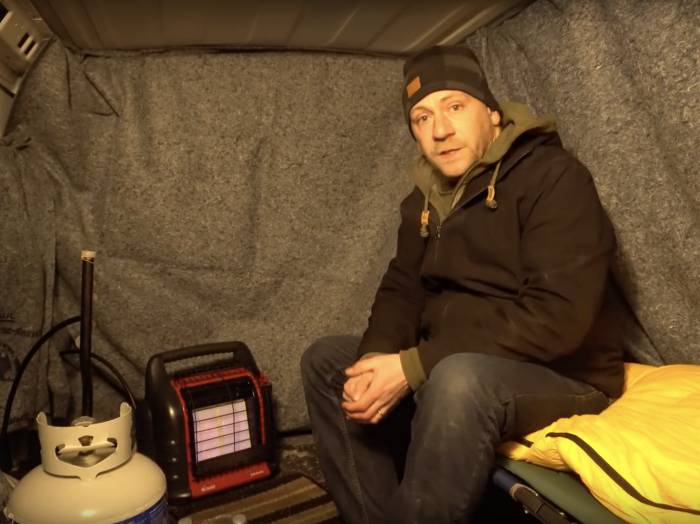 Steve Wallis sitting next to propane heater inside U-Haul talking to camera