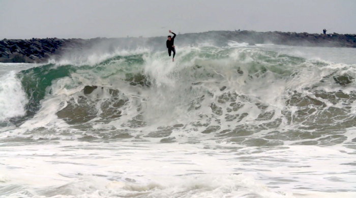 man in black wetsuit body surfing and leaping from frothy wave